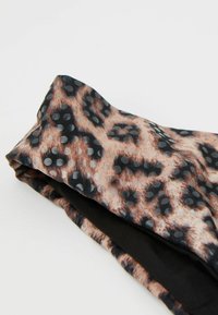 Gefalteter Stoff mit Leopardenmuster, bedeckt mit kleinen schwarzen erhabenen Punkten auf hellem Untergrund.