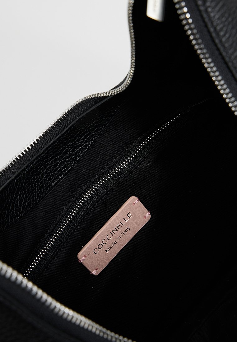 Intérieur d'un sac en cuir noir avec une fermeture éclair argentée et une étiquette rose cousue à l'intérieur indiquant "COCCINELLE Fabriqué en Italie."