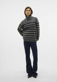 Pull à col roulé rayé gris avec des rayures horizontales noires, confectionné à partir d'un matériau doux, associé à un pantalon évasé bleu foncé.