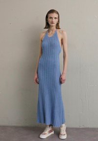 Robe midi bleu clair à rayures avec un col halter ; présente un buste ajusté et une jupe évasée. Associée à des baskets blanches.