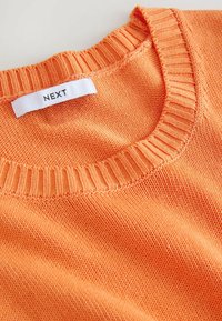 Maglione arancione lavorato a maglia con collo a girocollo a coste e l'etichetta "NEXT" cucita nel collo. Tessuto morbido con una sensazione leggera.