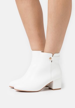 Bottines blanches en cuir lisse, dotées d'un talon bloc et d'une fermeture sécurisée avec un bouton sur le côté.