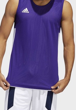 Homme portant un maillot de sport sans manches Adidas violet et un short de basketball blanc, tenant l'ourlet du maillot avec les deux mains.