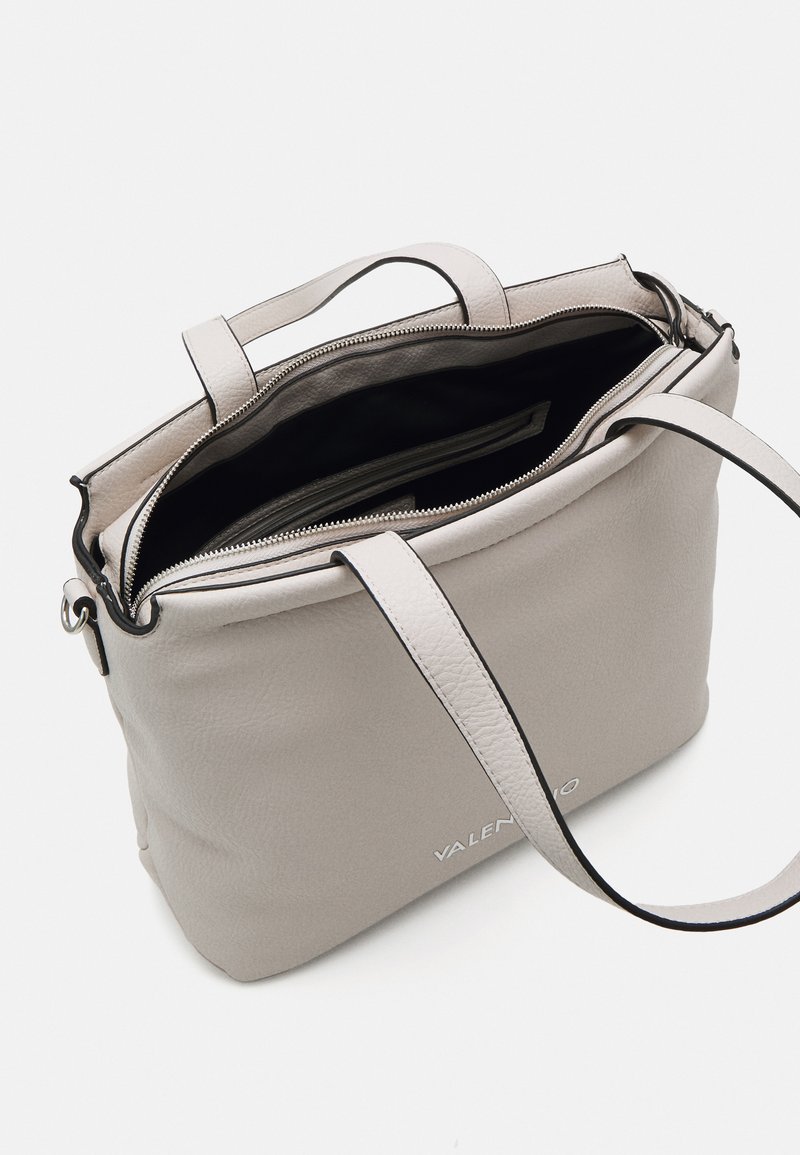 Bolso tote de cuero gris claro con cierre de cremallera, dos asas resistentes y forro interior negro; presenta un detalle del logo en la parte frontal.