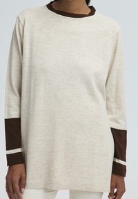Maglione a maniche lunghe color crema con colletto a coste marrone e maniche marroni a contrasto con strisce bianche ai polsini. Texture morbida.