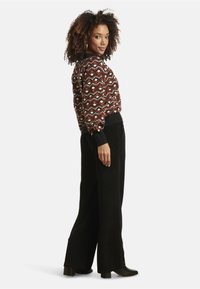 Patterned sweater in brown, red, and cream with geometric design; black high-waisted trousers; suede texture and chunky heeled boots.