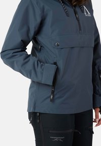 Marinblå vattentät jacka med halvdragkedja, som har en framficka, justerbara ärmslut och logotyper på bröstet och ärmen.