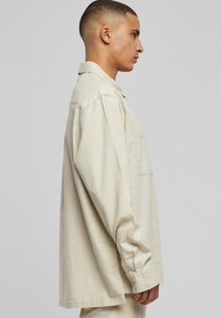Bézs overshirt, könnyű anyagból készült. Gallérral, hosszú ujjakkal és egy folt zsebbel rendelkezik. Laza fazon, egyenes vágású.