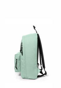Mochila verde menta con acentos negros, que cuenta con un bolsillo lateral, correas ajustables y una textura de tela suave. Diseño compacto y rectangular.