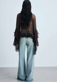Sheer black top with ruffled sleeves paired with light blue wide-leg jeans featuring frayed hems. Soft textures and flowing design.