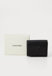 Juodas odinis piniginė su iškilniu "ck" logotipu, kompaktiškas dizainas, užsukamo tipo uždarymas. Pateikta baltoje dėžutėje, pažymėtoje "Calvin Klein".