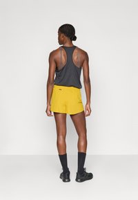Tumehall tank top racerback kujundusega, koos kollaste jooksuspordilühkaritega. Omadused sisaldavad elastset vööd ja keskmise reie pikkust.