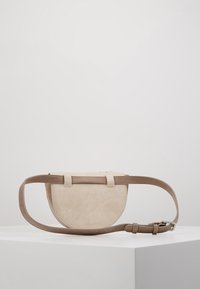 Béžová kožená crossbody taška, kulatého tvaru s texturovaným povrchem, se zapínáním na popruh a dvěma vertikálními popruhy. Minimalistický design.