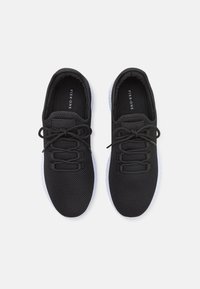 Černé sporty boty s síťovaným svrškem, kulatými tkaničkami, polstrovanou stélkou a bílou gumovou podrážkou, které mají minimalistický design.