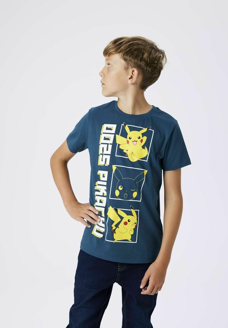 Lyhythihainen sininen t-paita, jossa on kolme keltaista ja mustaa Pikachu-kuvaa, sekä "025 Pikachu" -teksti sivulla. Sujuva puuvillakangas.