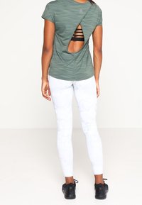 Grön atletisk tröja med en skörtdel på baksidan, kombinerad med vita leggings med marmor mönster och svarta sneakers. Slät tygtextur.