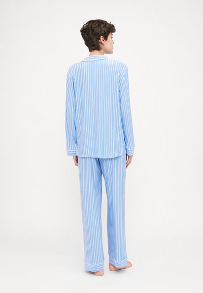 Conjunto de pijama listrado azul claro feito de tecido macio. Apresenta mangas longas, colarinho e calças folgadas com padrões de listras horizontais.