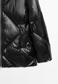 Black puffer jacket with shiny, quilted texture. Features diagonal stitching and a single patch pocket. Zipper closure at the front.