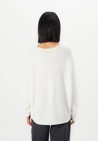 Light cream pullover sweater with a relaxed fit, wide sleeves, and a round neckline, featuring a central seam down the back.