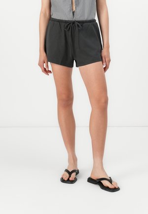 Black shorts with an elastic waist and drawstring. Smooth, lightweight fabric. Paired with black flip-flops and a textured gray top.