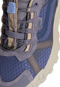 Niebiesko-szary but do wędrówek z teksturowaną cholewką, zamszowym i siateczkowym materiałem, wyściełanym kołnierzem oraz unikalnym systemem sznurowania z plastikowym zatrzaskiem.