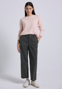 Maglione rosa chiaro con scollatura rotonda e maniche lunghe abbinato a pantaloni in velluto a coste grigio scuro con due bottoni frontali e una vestibilità morbida.