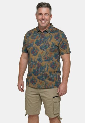 Uśmiechnięty mężczyzna w koszuli z krótkim rękawem i kołnierzykiem, zdobionej wzorem rafy koralowej, oraz w beżowych szortach typu cargo z kieszeniami na zamek i patkę.