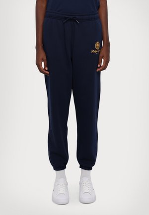 Marineblaue Jogginghose mit elastischen Bündchen, Kordelzugbund, goldenem Ralph Lauren-Logo am Oberschenkel, getragen mit weißen Socken und weißen Sneakers.