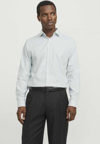 Camicia a maniche lunghe azzurra, con bottoni e colletto a punta, realizzata in tessuto liscio. Abbinata a pantaloni neri plissettati e una cintura nera.