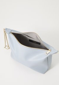 Borsa di pelle azzurro chiaro con chiusura a zip dorata, tracolla a catena e interno in tessuto grigio con etichetta. Texture liscia e forma strutturata.