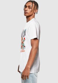 Hvid bomulds T-shirt med et farverigt grafisk design på fronten, der skildrer en kæreste med penge og blomstermotiver. Standard pasform.