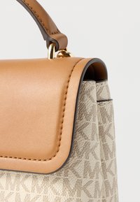 Strukturalna torebka o fakturowanej beżowej powierzchni z subtelnym geometrycznym wzorem, uzupełniona gładkim jasnobrązowym skórzanym wierzchem i złotymi okuciami.