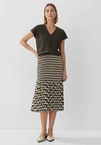 Maglietta verde scuro a scollo a V abbinata a una gonna midi plissettata a motivi geometrici beige e neri. Scarpe beige completano l'outfit.