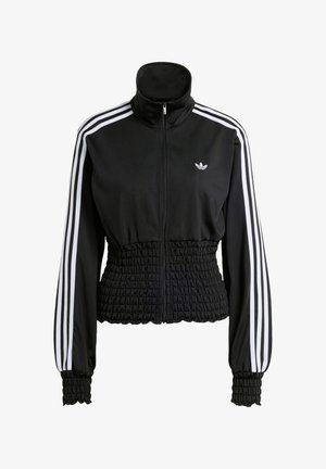 Crna sportska jakna s visokim ovratnikom, patent zatvaračem duž cijele duljine i elastičnim pojasom u struku. Ima bijele pruge na ramenima i rebraste manžete. Prikazan je Adidasov logo.