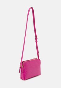 Różowa torebka na ramię z tłoczonym wzorem krokodyla, o płaskim kształcie, z dwoma przegrodami zamykanymi na suwak oraz regulowanym paskiem. Gładka faktura z elementami w kolorze złotym.