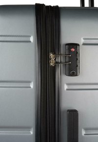 Maleta rígida plateada con un acabado texturizado, cremalleras negras, cerradura TSA y mango retráctil visible en el lateral.