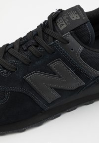 Sneaker din suede negru și plasă cu o suprafață texturată, având un logo "N" negru proeminent și șireturi negre asortate pe o talpă din cauciuc.