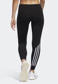 Mustat urheiluleggingsit korkealla vyötäröllä, joissa on valkoiset pystysuorat raidat sivuilla ja sileä, joustava materiaali.