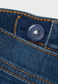 Denimtyg i djupblått med synlig sömnad i en kontrasterande orange. Har en klar knapp och ett vävt band i midjan.