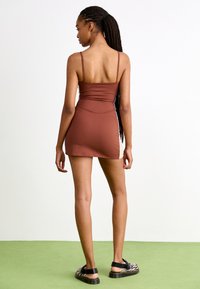 Ruda spaghetti dirželių suknelė su prigludusia viršutine dalimi ir platėjančia sijonu, pagaminta iš lygios medžiagos. Dėvima su juodai baltomis raštuotomis šlepetėmis.