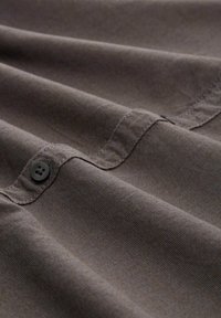 Material maro cu o suprafață texturată, având cusături vizibile, un nasture și variații subtile de culoare. Materialul pare a fi durabil.