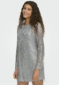 Vestido plateado con lentejuelas y mangas largas, que presenta detalles de flecos verticales, escote redondo y forma ajustada. Material suave con brillo.