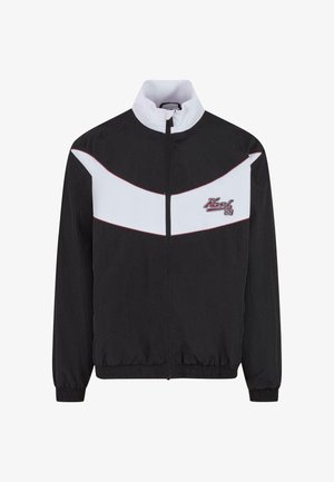 Mustmustern musta jope, millel on valge chevron muster ja punased aktsendid. Sellel on tõusnud krae ning elastne mansett ja äär.