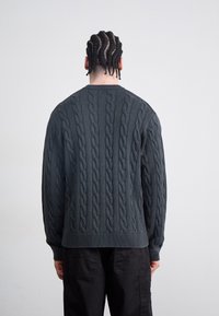 Pulover din lână tricotat în gri închis, cu un design texturat, decolteu rotund și manșete și tiv cu elastic. Vedere din spate care evidențiază detaliile modelului.