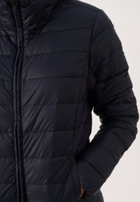 Marineblaue Steppjacke mit Reißverschluss, horizontal gesteppt, mit hoch geschlossenem Kragen und seitlichen Taschen. Glatte, glänzende Textur.