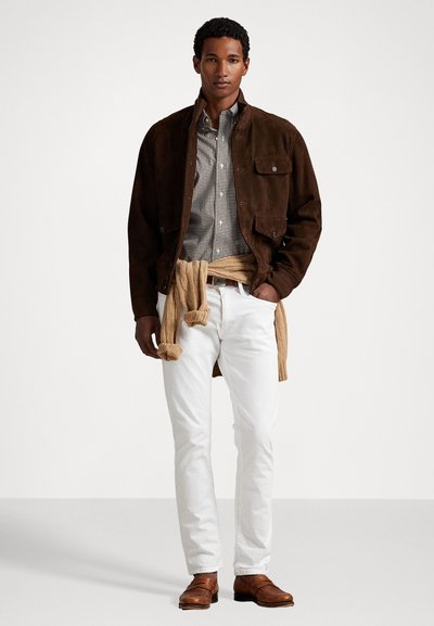Brown suede jacket over a striped button-down shirt, white jeans, and a knitted tan sweater tied at the waist. Brown leather shoes.