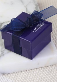 Paarse geschenkenbox met een glanzende afwerking en een donkerblauwe strik, met de tekst "Lucardi juwelier" in zilver. Geplaatst op een marmeren achtergrond.