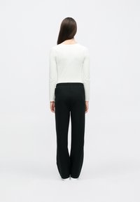 Λευκό τοπ με μακριά μανίκια σε συνδυασμό με μαύρο παντελόνι με ελαστική μέση, με χαλαρή γραμμή και ίσια ποδιά, εμφανιζόμενο από πίσω.