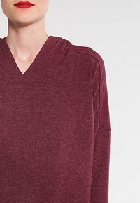 Burgundy pullover with a v-neck and hood, featuring a soft texture and long sleeves, displaying a subtle knit pattern.