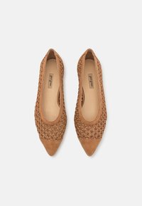 Ballerines beiges avec une tige tissée et un nez pointu. Le bout est en daim lisse, contrastant avec le design texturé du reste.
